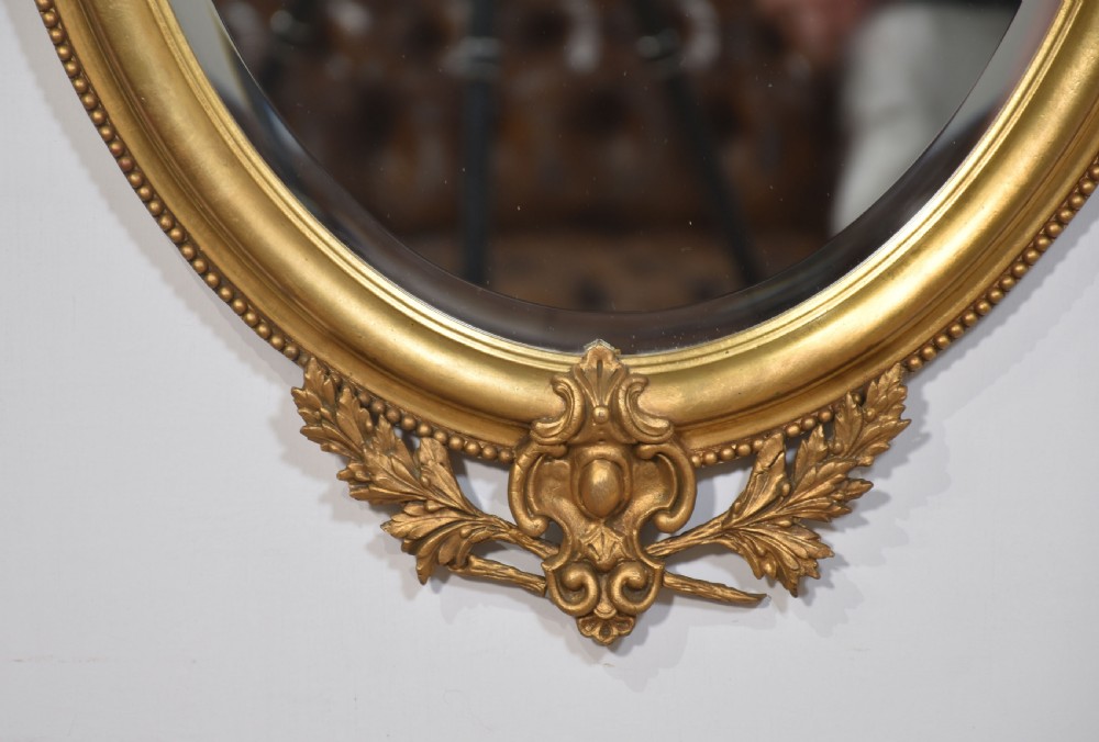 A matching pair of giltwood oval wall mirrors featuring classical urn finials with wheat ears, beaded side festoons, and scrolling leaf bottom aprons. View VIII