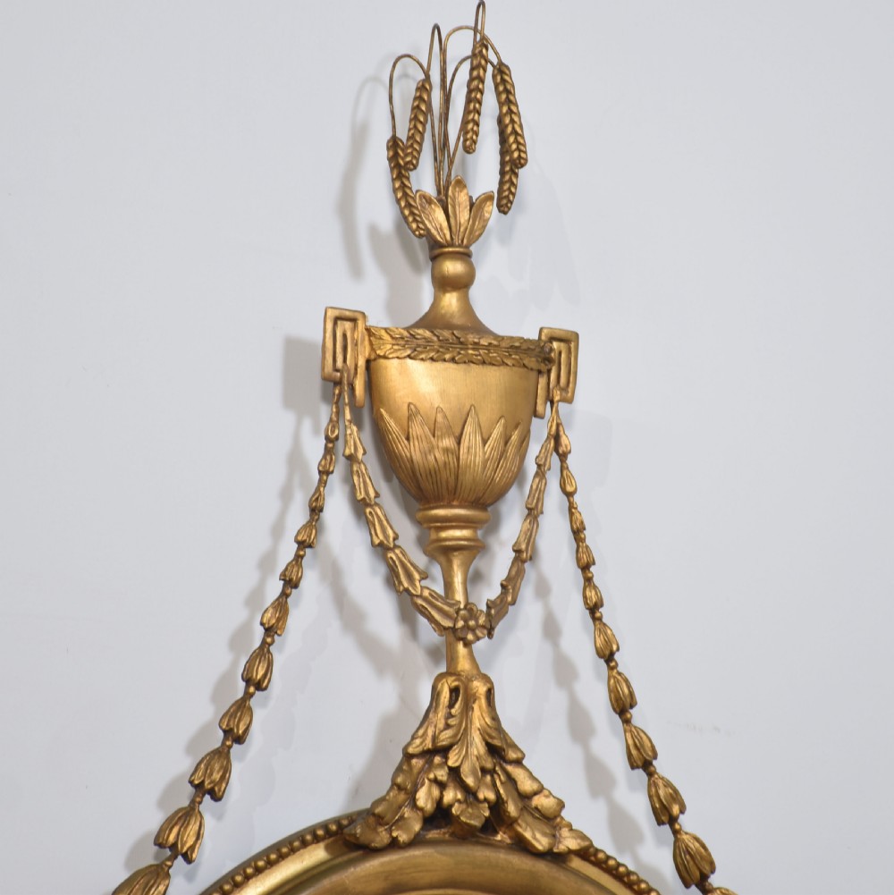 A matching pair of giltwood oval wall mirrors featuring classical urn finials with wheat ears, beaded side festoons, and scrolling leaf bottom aprons. View IX