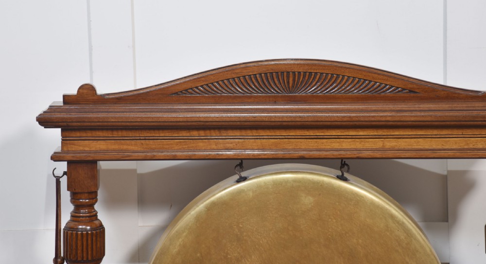 A freestanding Victorian walnut frame featuring turned columns, a carved cresting rail, and a central suspended circular brass gong disc with a side striker. View II