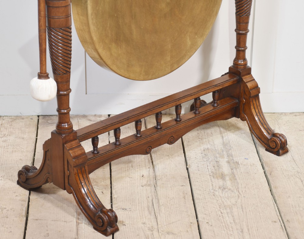 A freestanding Victorian walnut frame featuring turned columns, a carved cresting rail, and a central suspended circular brass gong disc with a side striker. View VI