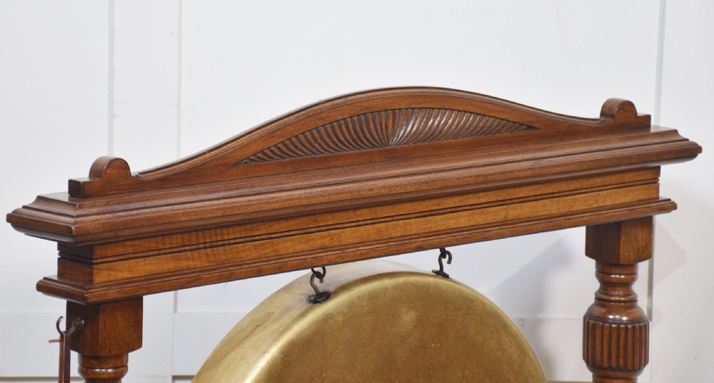 A freestanding Victorian walnut frame featuring turned columns, a carved cresting rail, and a central suspended circular brass gong disc with a side striker. View VII