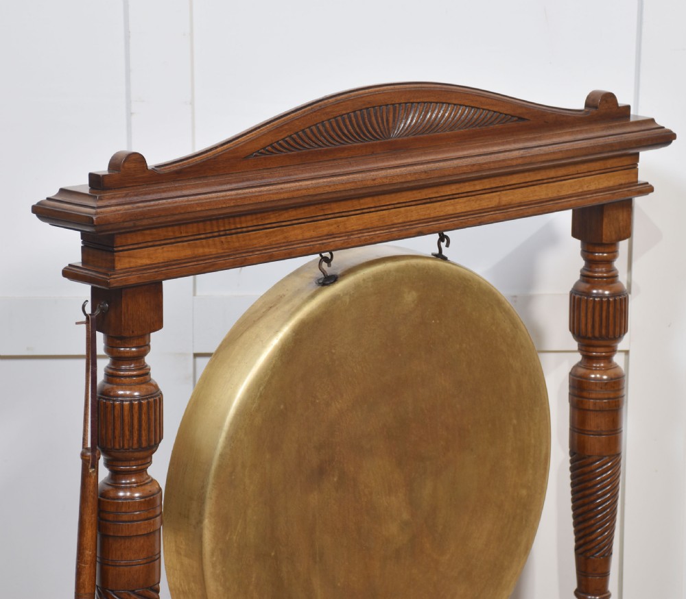 A freestanding Victorian walnut frame featuring turned columns, a carved cresting rail, and a central suspended circular brass gong disc with a side striker. View VIII