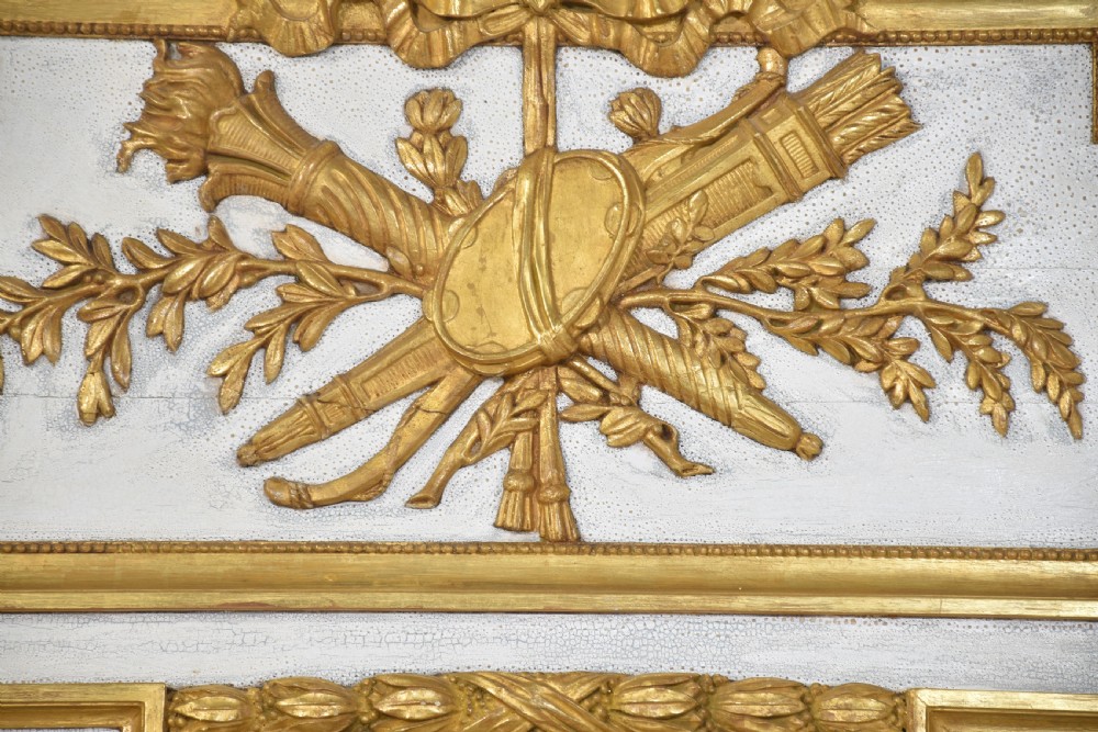 A tall French trumeau wall mirror with a painted white frame, gold leaf parcel gilding, a ribbon cresting top panel, and a rectangular glass mirror. View VI