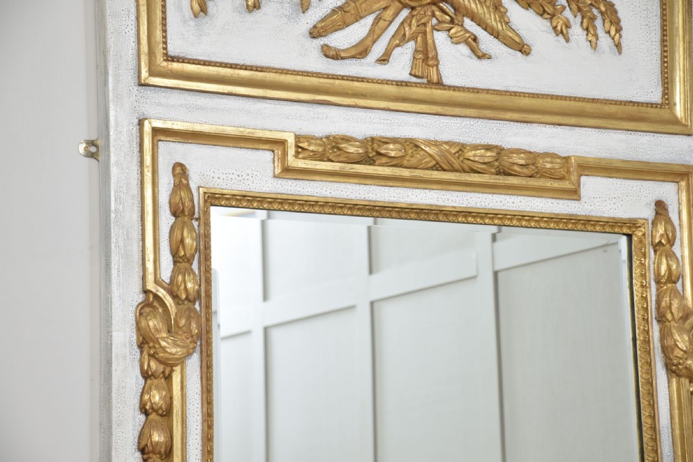 A tall French trumeau wall mirror with a painted white frame, gold leaf parcel gilding, a ribbon cresting top panel, and a rectangular glass mirror. View VII