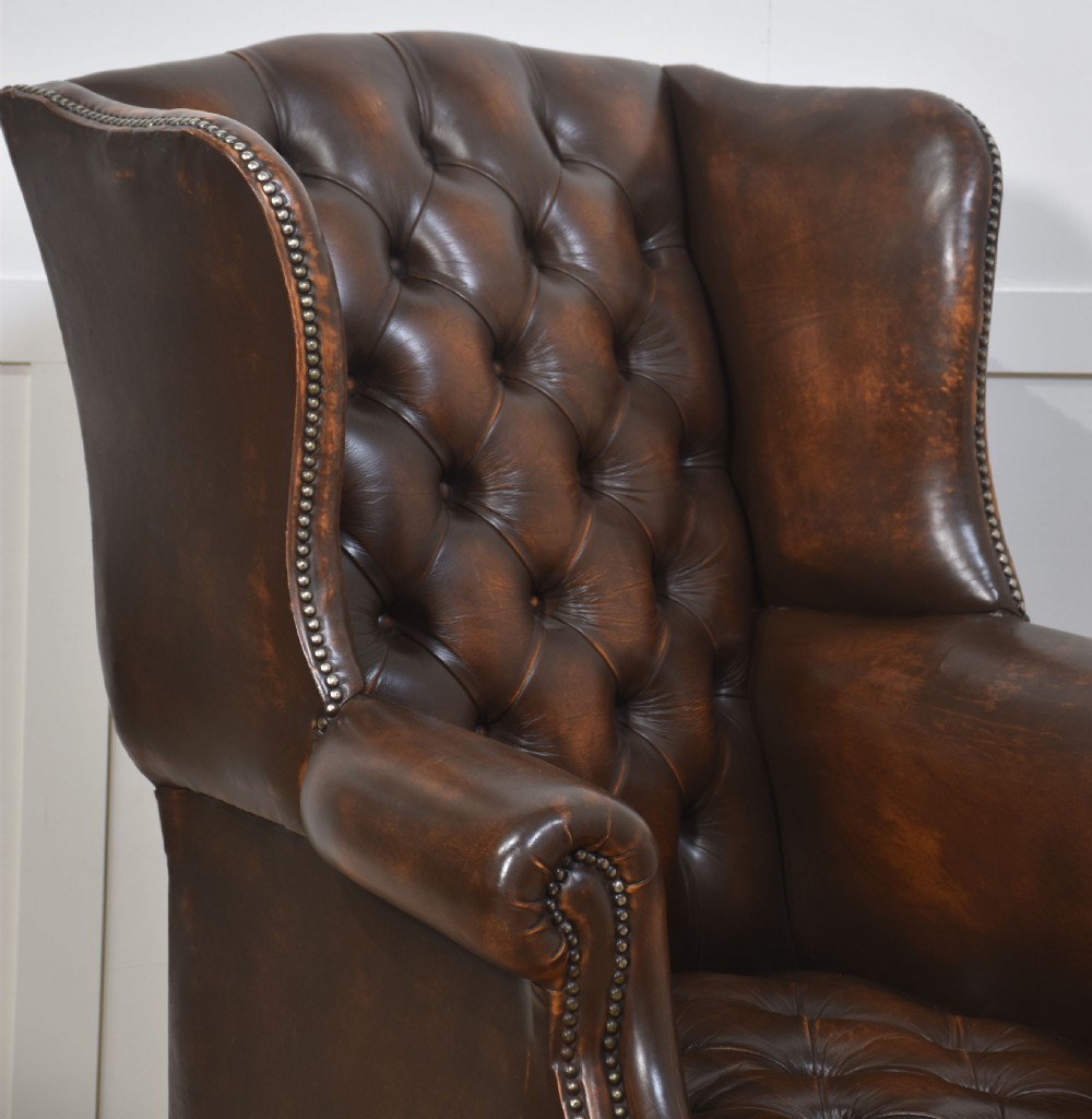 A warm brown leather wingback armchair with deep buttoned tufting, brass stud detailing, and dark wooden legs. View III