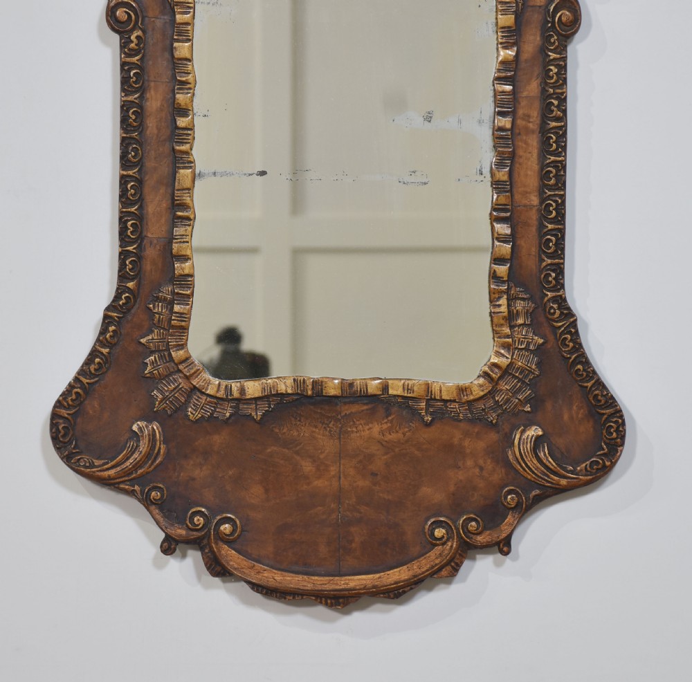 A George II style carved walnut wall mirror featuring a carved floral crest, parcel gilt trim, and a shaped apron surround. View III