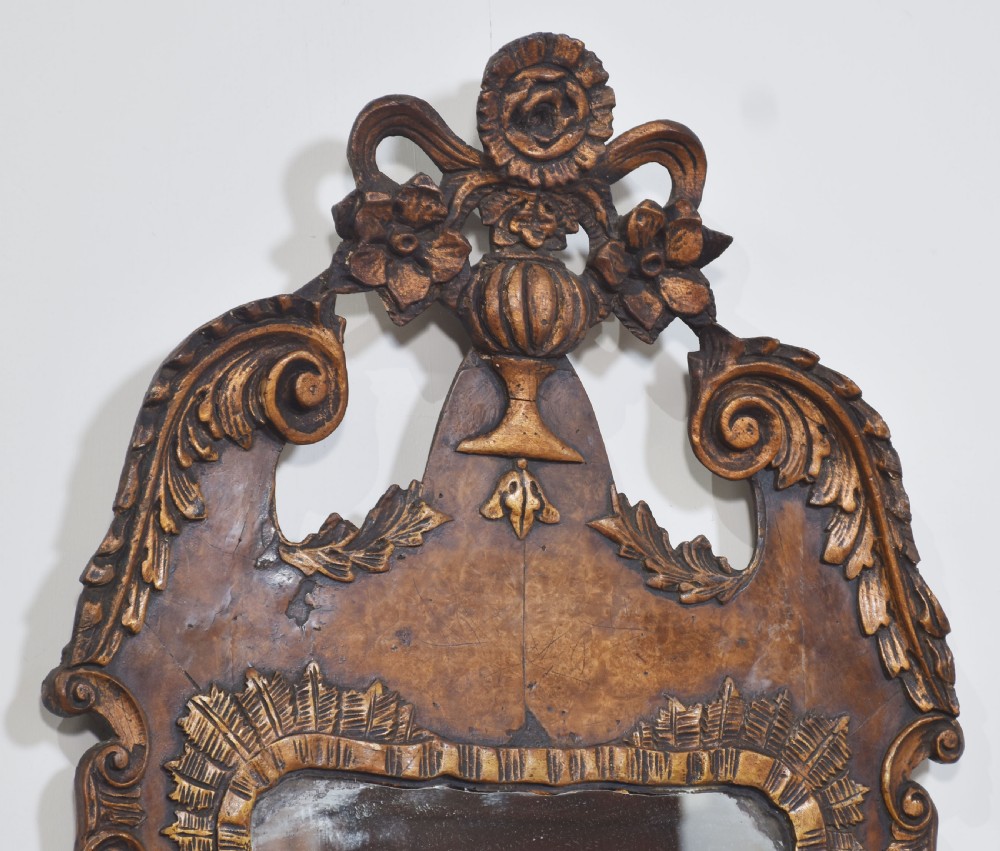 A George II style carved walnut wall mirror featuring a carved floral crest, parcel gilt trim, and a shaped apron surround. View VII