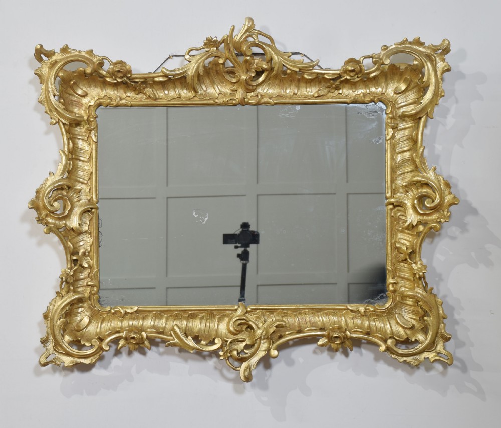 A 19th-century rectangular wall mirror featuring an ornate giltwood frame carved with Rococo C-scrolls and floral motifs.