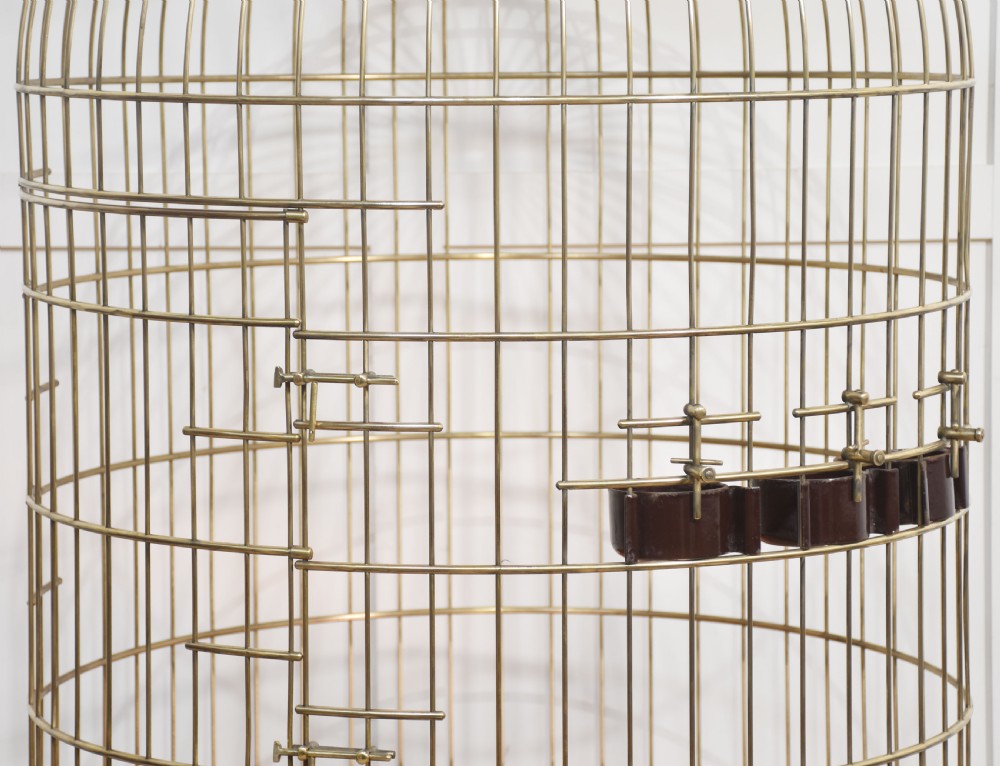 A large brass domed bird cage with a polished copper basin resting upon a grey wrought iron scrollwork stand. View II
