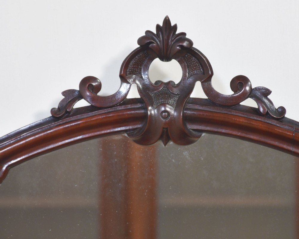 A Victorian mahogany duchess dressing table featuring an arch-topped swivel mirror flanked by carved uprights above a serpentine front desk with drawers and a shaped platform base. View II