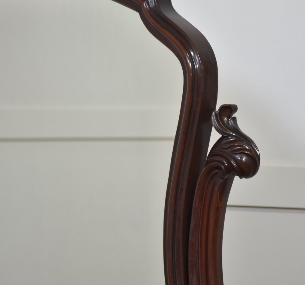 A Victorian mahogany duchess dressing table featuring an arch-topped swivel mirror flanked by carved uprights above a serpentine front desk with drawers and a shaped platform base. View X