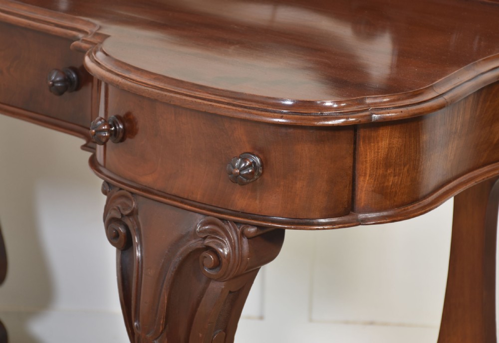 A Victorian mahogany duchess dressing table featuring an arch-topped swivel mirror flanked by carved uprights above a serpentine front desk with drawers and a shaped platform base. View XI