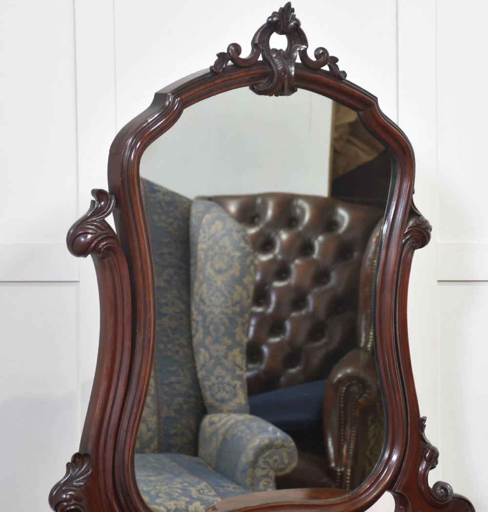 A Victorian mahogany duchess dressing table featuring an arch-topped swivel mirror flanked by carved uprights above a serpentine front desk with drawers and a shaped platform base. View XIII