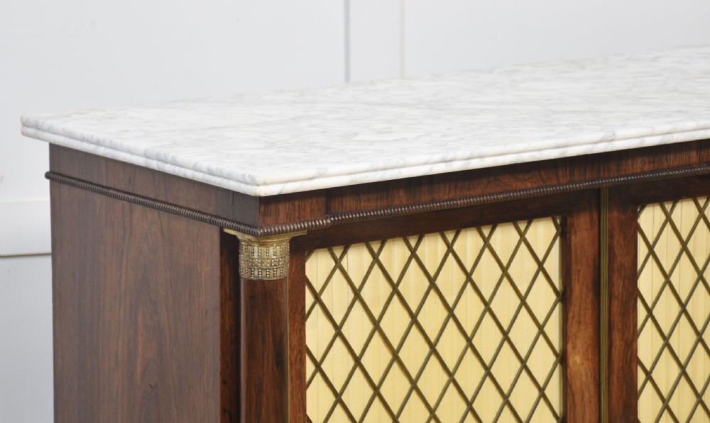 A nineteenth-century dark rosewood two-door cabinet featuring a white marble top, brass grille doors with pleated fabric lining, and columnar side supports. View VII
