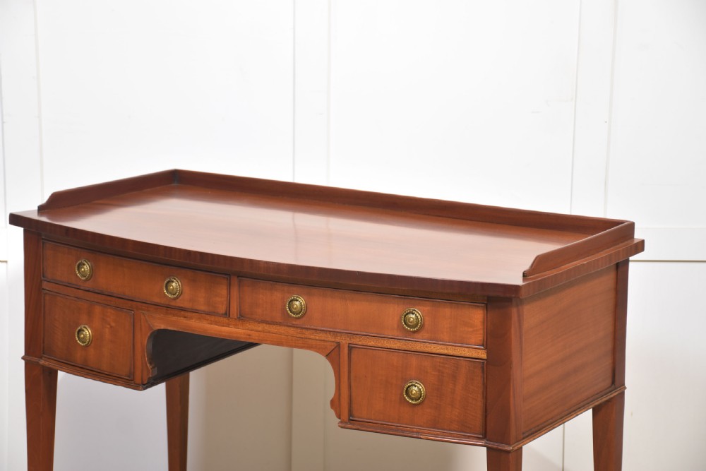 An antique warm brown mahogany writing table featuring a low gallery top, four drawers with circular brass pulls, tapered square legs, and brass castors. View VI
