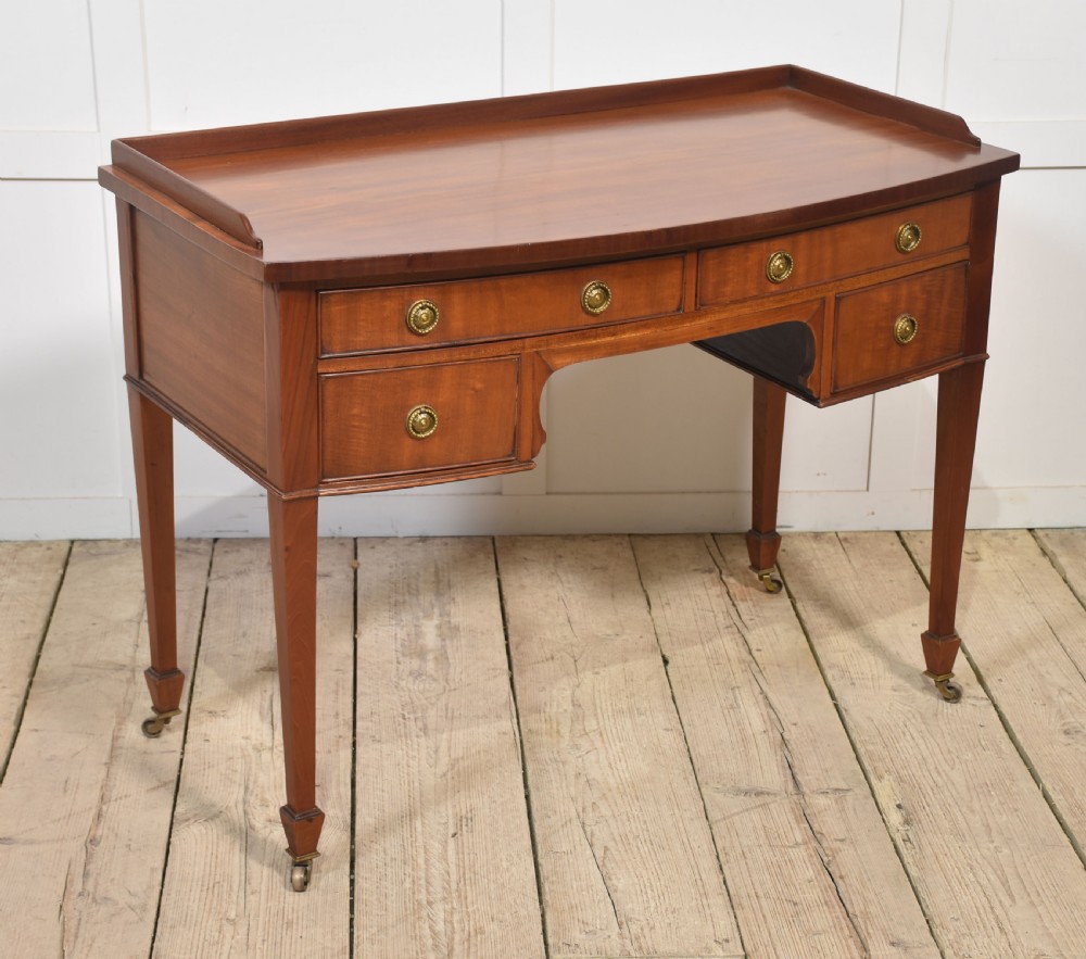 An antique warm brown mahogany writing table featuring a low gallery top, four drawers with circular brass pulls, tapered square legs, and brass castors. View IX