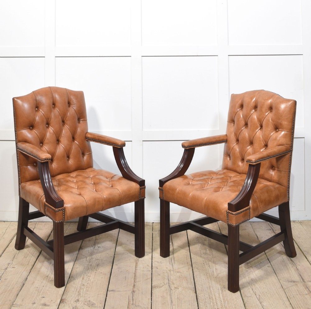 A pair of Georgian style tan leather Gainsborough library chairs featuring deep buttoned upholstery, brass studding, and dark mahogany frames.