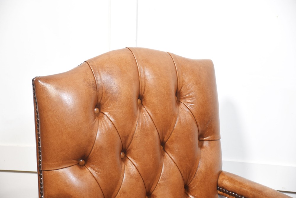 A pair of Georgian style tan leather Gainsborough library chairs featuring deep buttoned upholstery, brass studding, and dark mahogany frames. View V