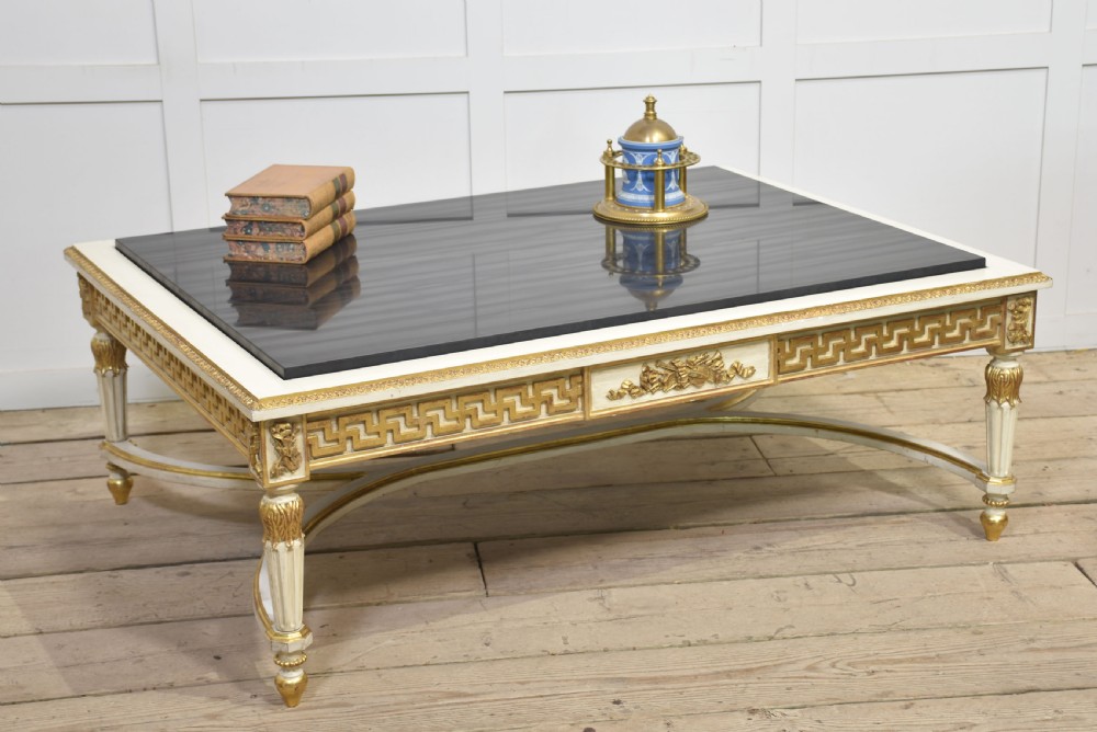 A low rectangular Venetian style coffee table featuring a black stone top, cream painted frieze with gold Greek key carving, and parcel gilt fluted legs. View II
