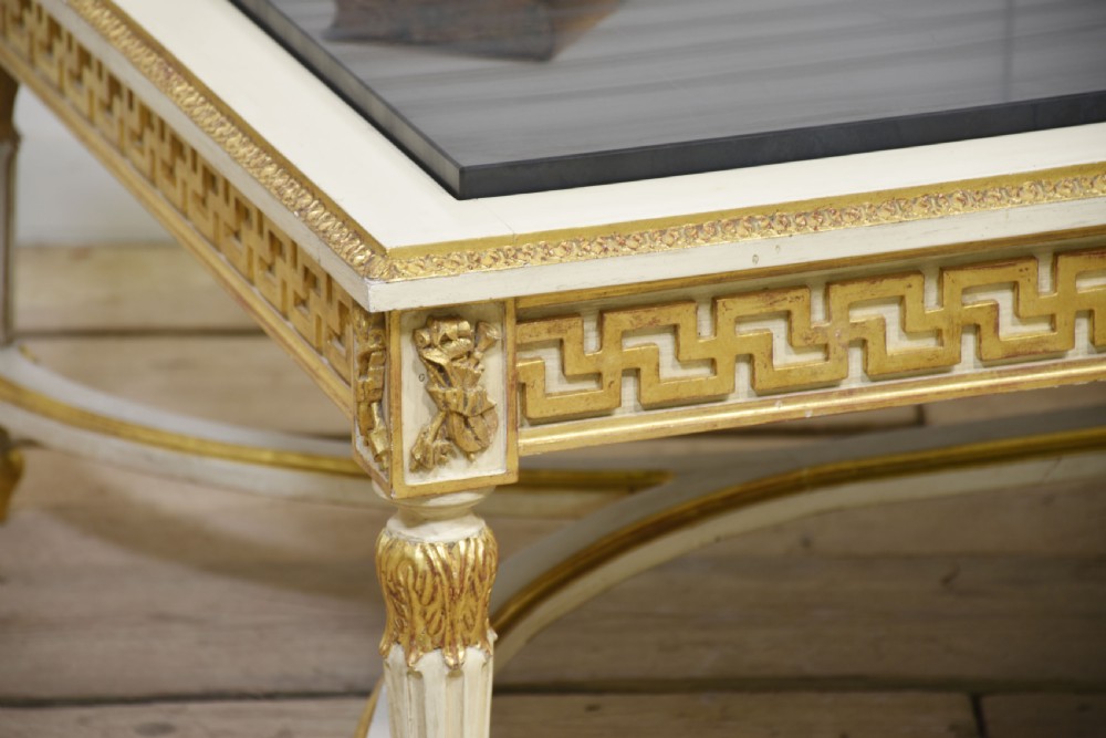 A low rectangular Venetian style coffee table featuring a black stone top, cream painted frieze with gold Greek key carving, and parcel gilt fluted legs. View III