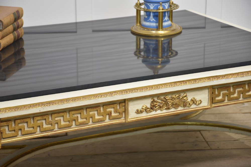 A low rectangular Venetian style coffee table featuring a black stone top, cream painted frieze with gold Greek key carving, and parcel gilt fluted legs. View V