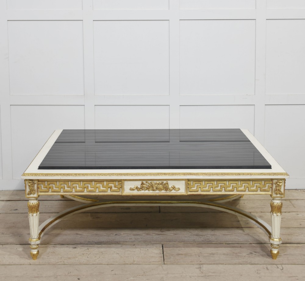 A low rectangular Venetian style coffee table featuring a black stone top, cream painted frieze with gold Greek key carving, and parcel gilt fluted legs. View VI