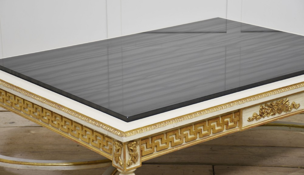 A low rectangular Venetian style coffee table featuring a black stone top, cream painted frieze with gold Greek key carving, and parcel gilt fluted legs. View XII