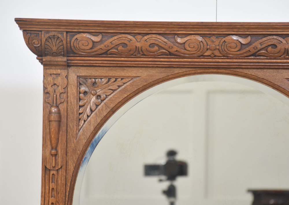 An antique carved oak cheval mirror featuring an arched glass plate supported by turned upright columns on a solid plinth base. View II