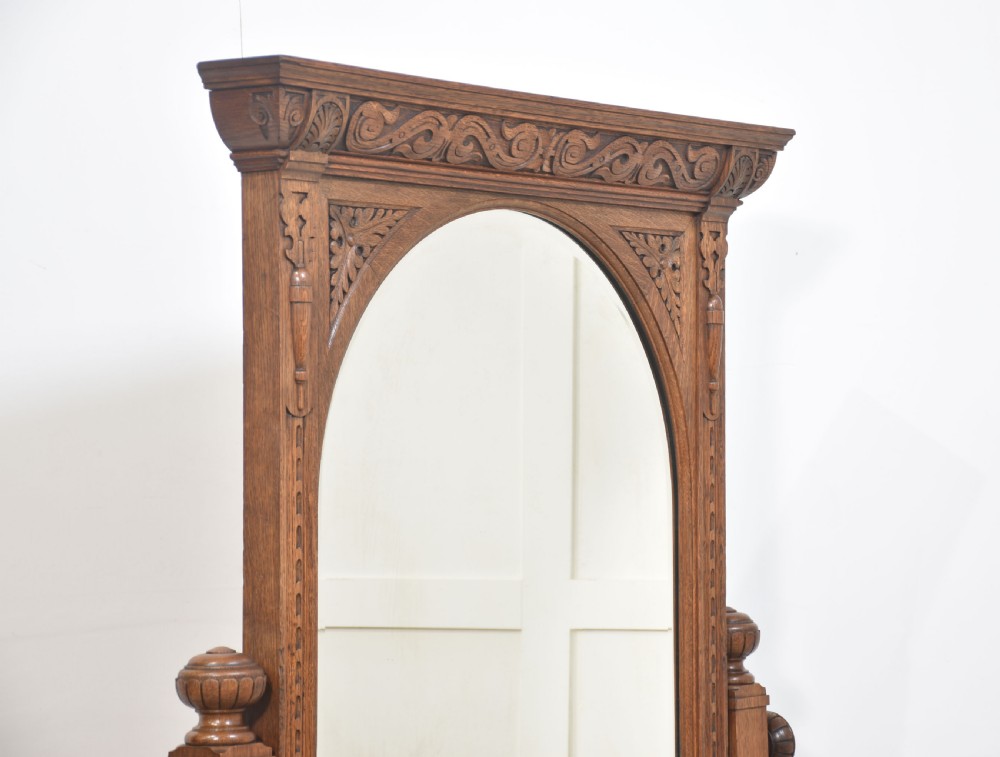 An antique carved oak cheval mirror featuring an arched glass plate supported by turned upright columns on a solid plinth base. View V