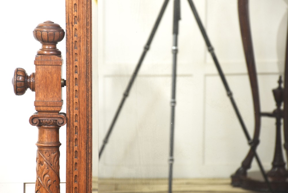 An antique carved oak cheval mirror featuring an arched glass plate supported by turned upright columns on a solid plinth base. View VI