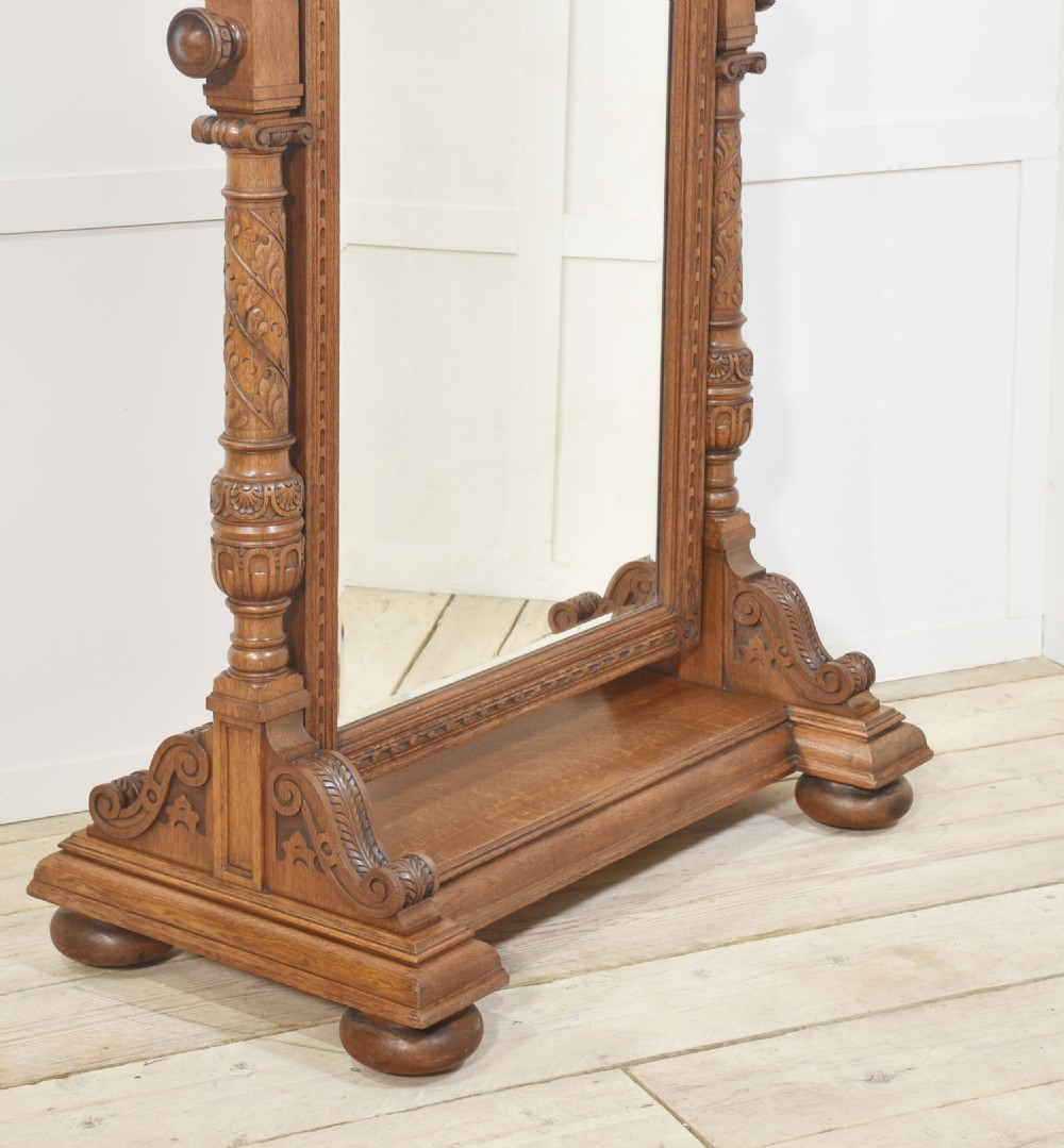 An antique carved oak cheval mirror featuring an arched glass plate supported by turned upright columns on a solid plinth base. View VIII