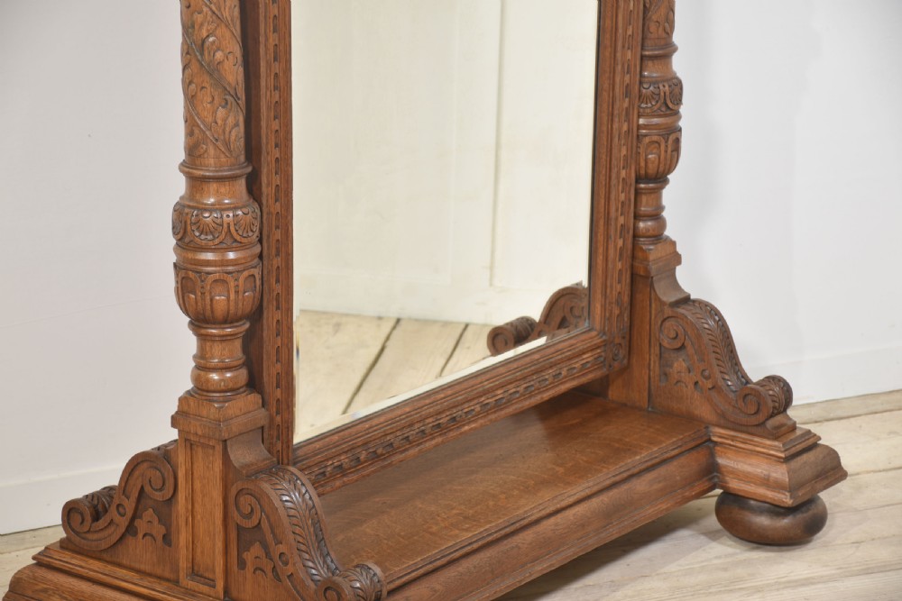 An antique carved oak cheval mirror featuring an arched glass plate supported by turned upright columns on a solid plinth base. View IX