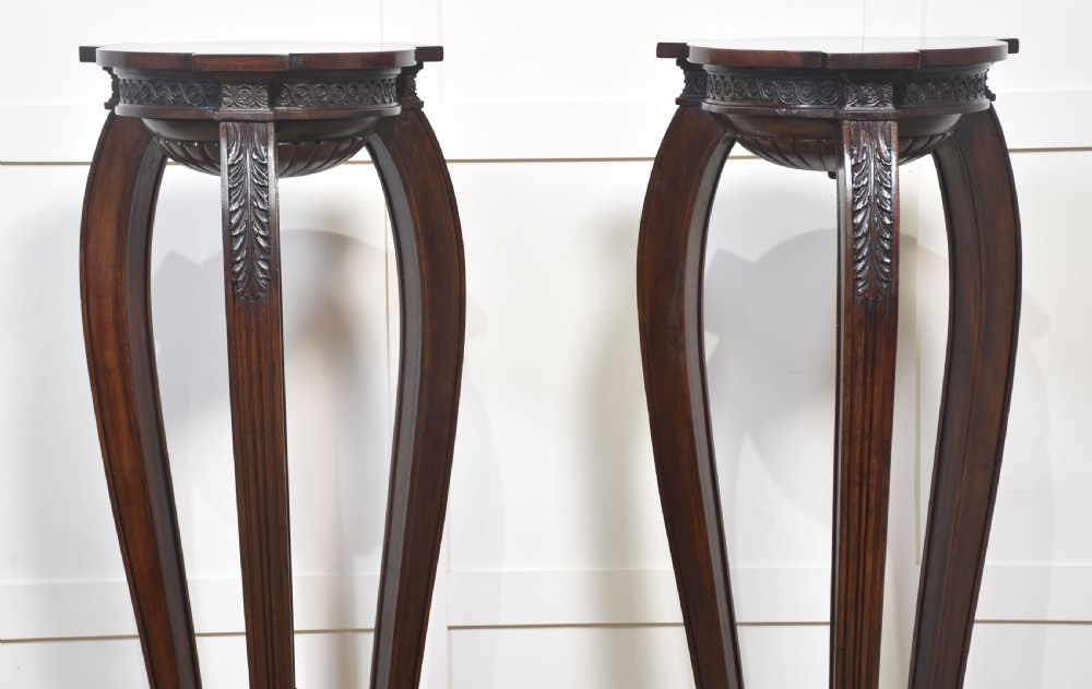 A pair of tall carved mahogany torchere plant stands featuring curved legs, carved foliage details, lower stretchers with finials, and circular bases. View III