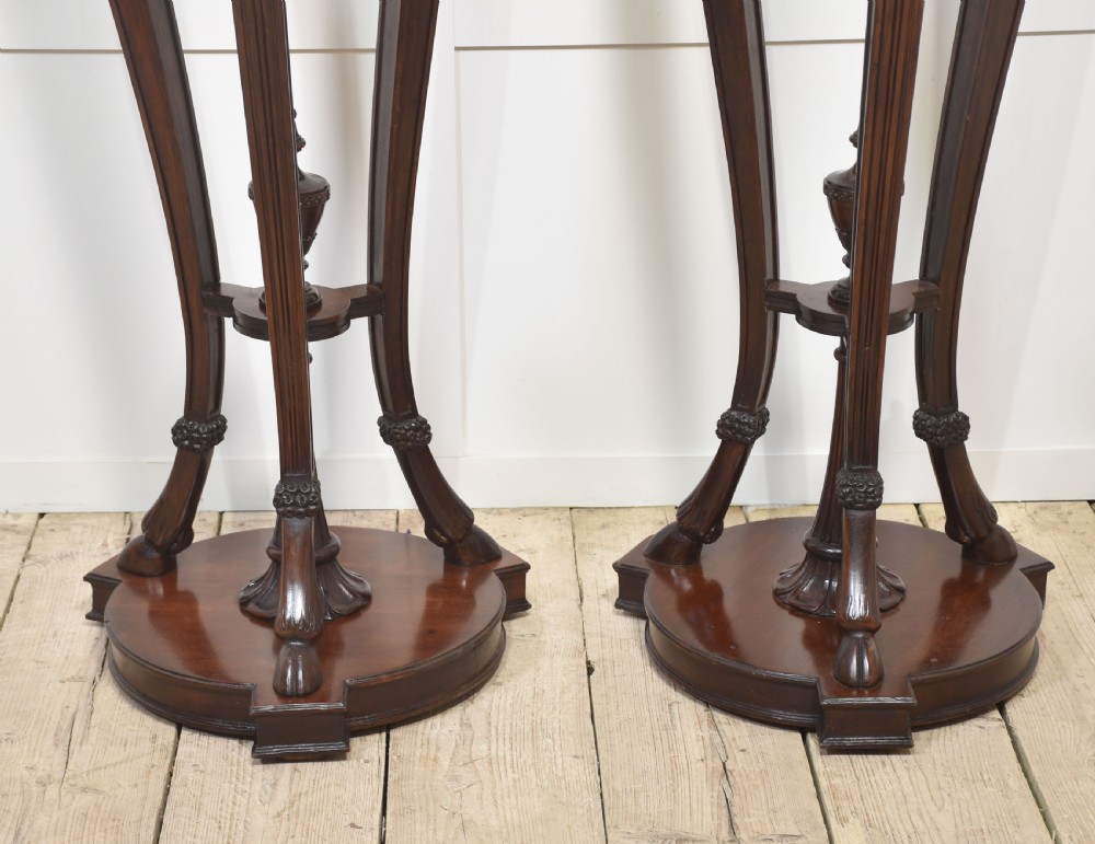 A pair of tall carved mahogany torchere plant stands featuring curved legs, carved foliage details, lower stretchers with finials, and circular bases. View V