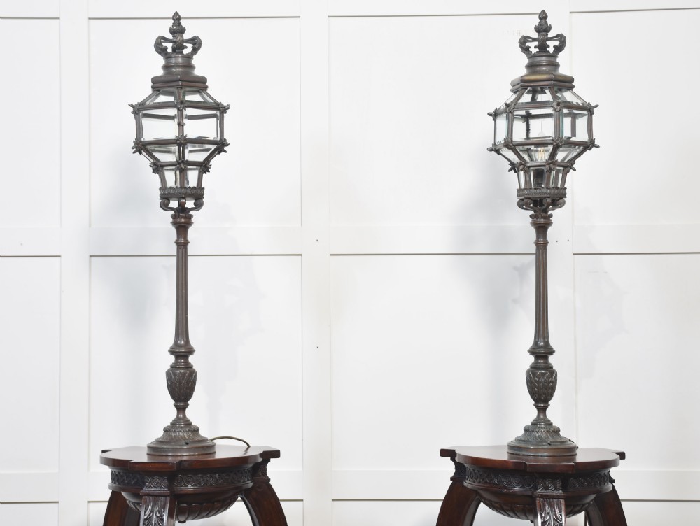 A pair of tall dark bronze newel post lamps featuring glazed hexagonal lanterns topped with decorative crown finials.