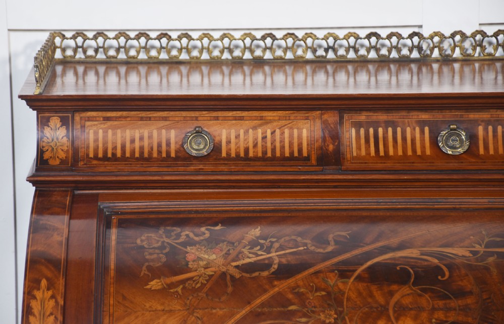 A Sheraton Revival mahogany cylinder bureau featuring intricate marquetry inlays on the curved roll-top lid, a brass gallery top, three drawers, and tapered legs. View III