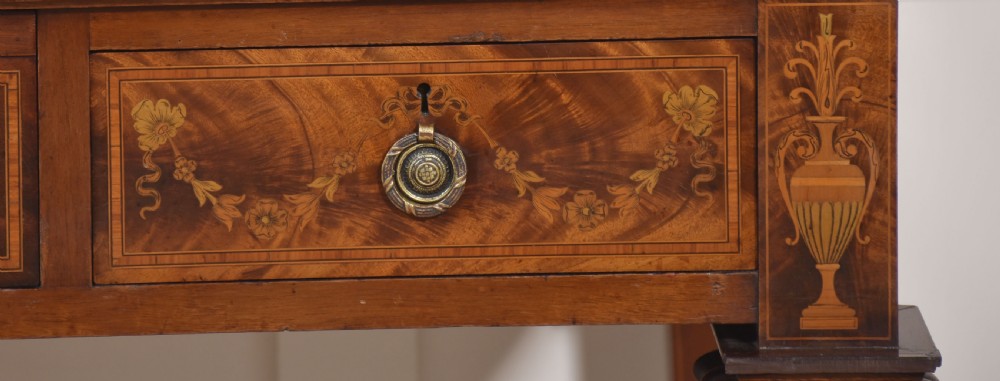 A Sheraton Revival mahogany cylinder bureau featuring intricate marquetry inlays on the curved roll-top lid, a brass gallery top, three drawers, and tapered legs. View VII