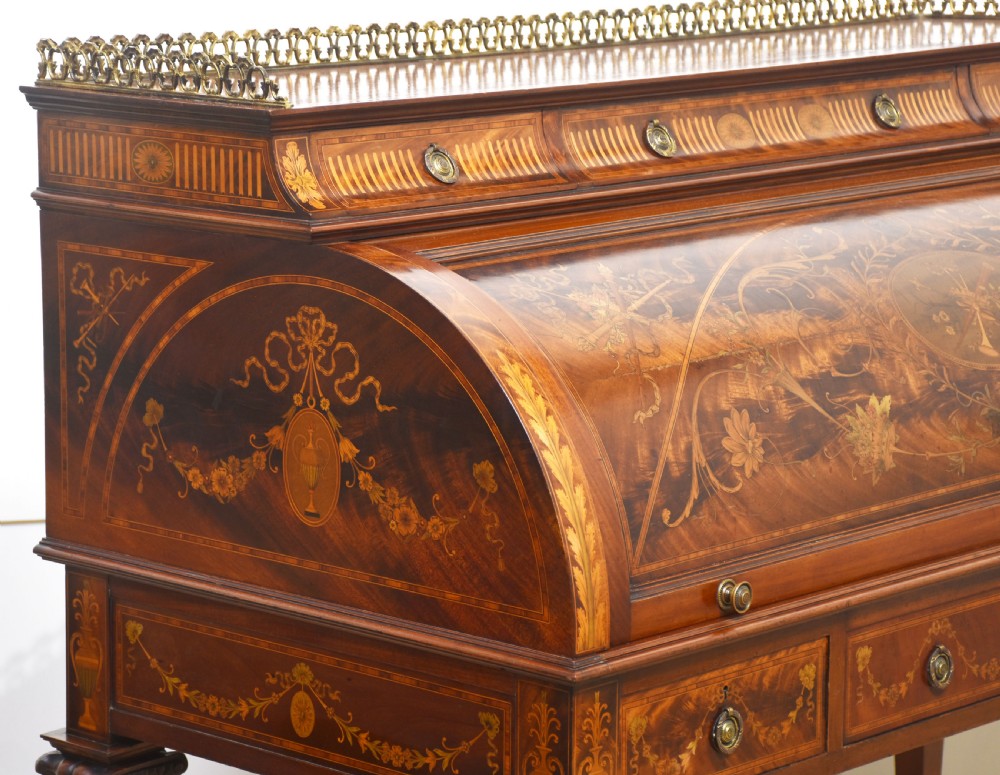 A Sheraton Revival mahogany cylinder bureau featuring intricate marquetry inlays on the curved roll-top lid, a brass gallery top, three drawers, and tapered legs. View IX
