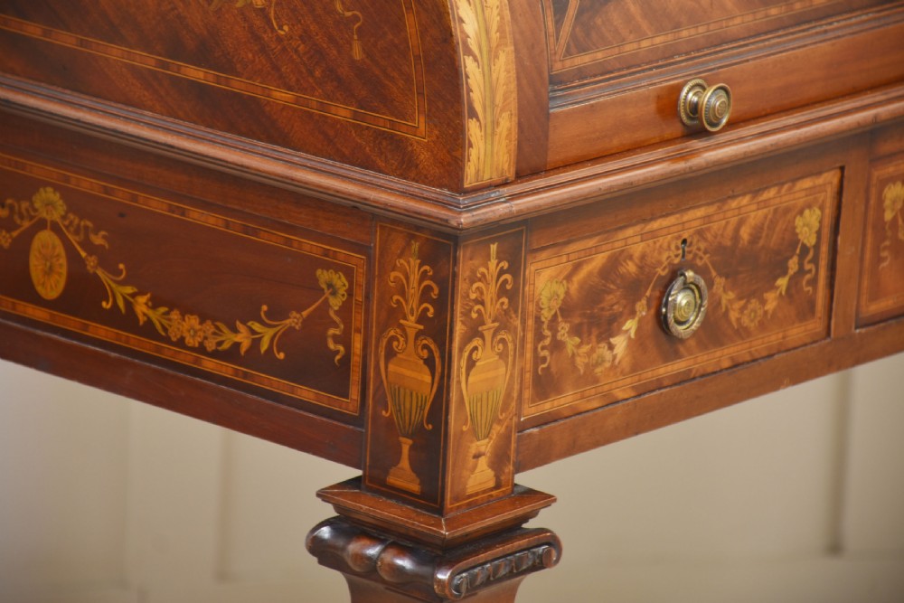 A Sheraton Revival mahogany cylinder bureau featuring intricate marquetry inlays on the curved roll-top lid, a brass gallery top, three drawers, and tapered legs. View X