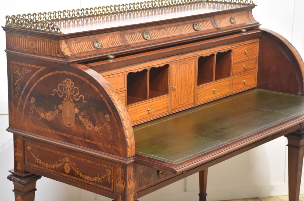 A Sheraton Revival mahogany cylinder bureau featuring intricate marquetry inlays on the curved roll-top lid, a brass gallery top, three drawers, and tapered legs. View XIII