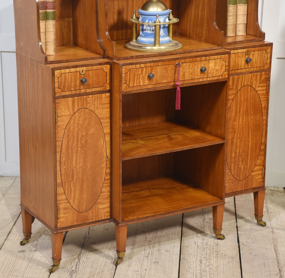 A matching pair of open satinwood breakfront bookcases featuring stepped waterfall shelving, inlaid drawers, and oval panel cupboard doors. View VI