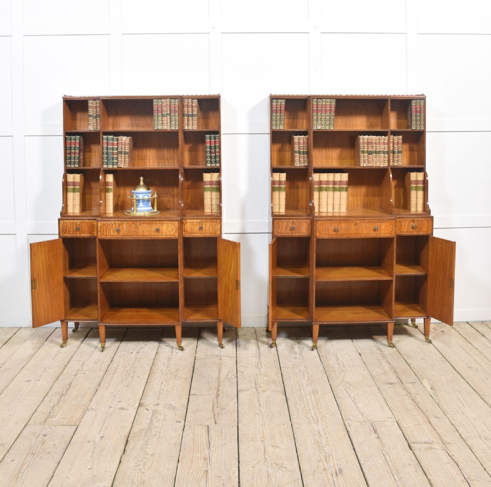 A matching pair of open satinwood breakfront bookcases featuring stepped waterfall shelving, inlaid drawers, and oval panel cupboard doors. View X