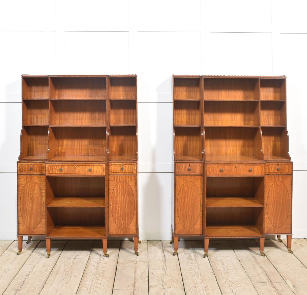 A matching pair of open satinwood breakfront bookcases featuring stepped waterfall shelving, inlaid drawers, and oval panel cupboard doors. View XII