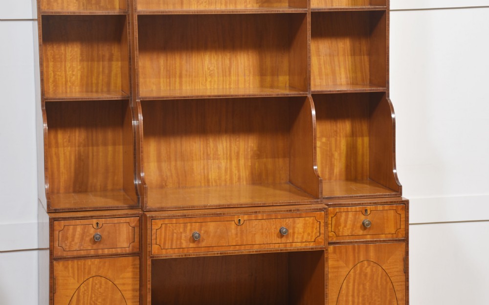 A matching pair of open satinwood breakfront bookcases featuring stepped waterfall shelving, inlaid drawers, and oval panel cupboard doors. View XIII