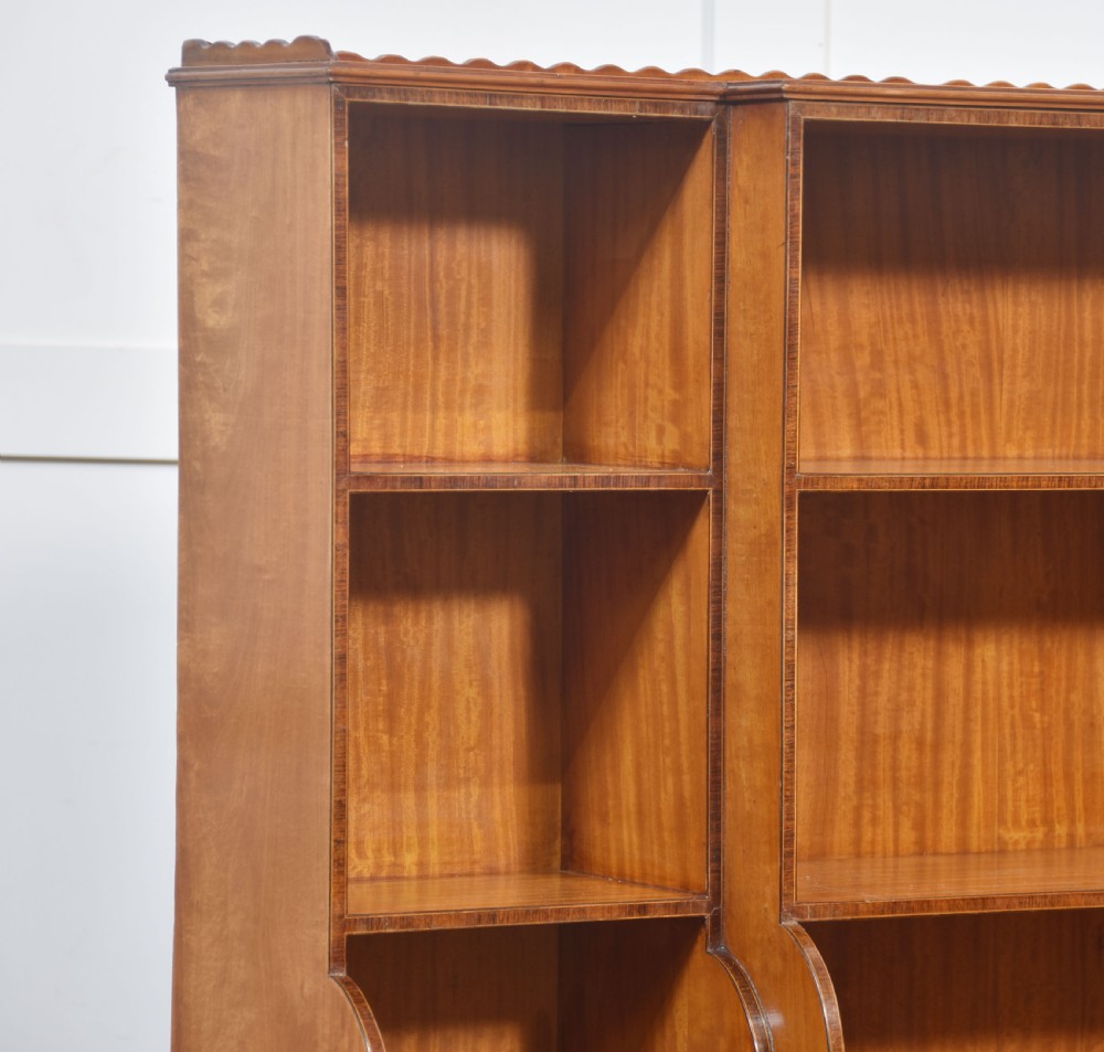 A matching pair of open satinwood breakfront bookcases featuring stepped waterfall shelving, inlaid drawers, and oval panel cupboard doors. View XVII