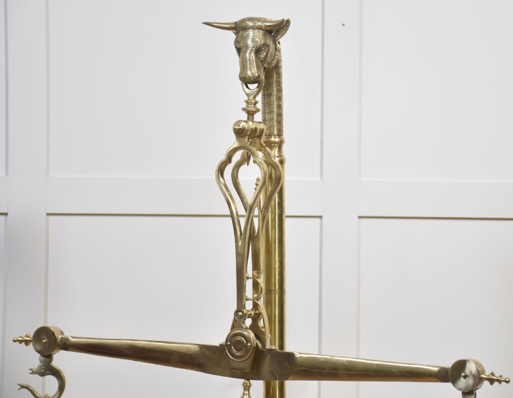 A floor-standing brass balance scale featuring a bull head finial, turned central column, horizontal beam, and two circular brass pans suspended by chains. View II