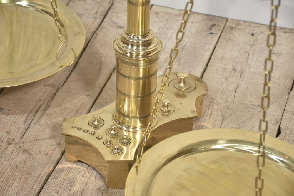 A floor-standing brass balance scale featuring a bull head finial, turned central column, horizontal beam, and two circular brass pans suspended by chains. View VII