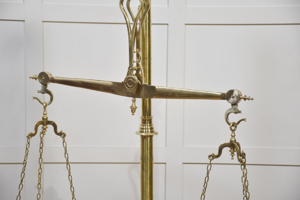 A floor-standing brass balance scale featuring a bull head finial, turned central column, horizontal beam, and two circular brass pans suspended by chains. View VIII