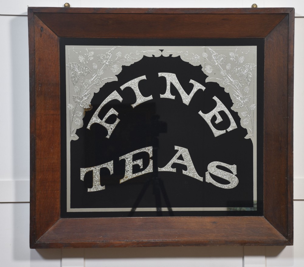 A square Victorian advertising mirror framed in dark wood, featuring silvered arched lettering reading FINE TEAS on a black painted glass ground.