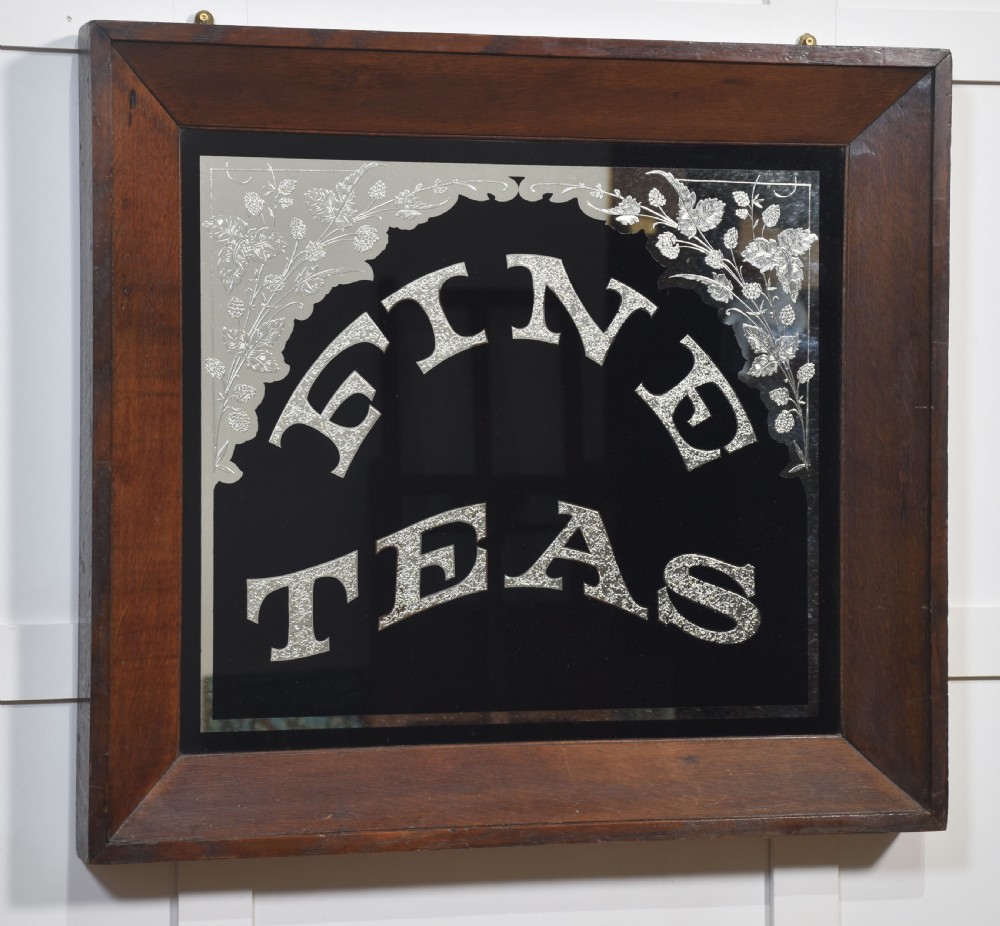 A square Victorian advertising mirror framed in dark wood, featuring silvered arched lettering reading FINE TEAS on a black painted glass ground. View V